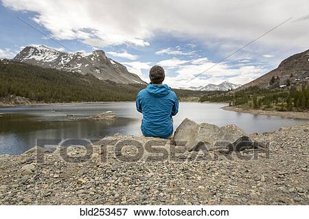 Stock Photo - Caucasian man sitting on rock near lake. Fotosearch