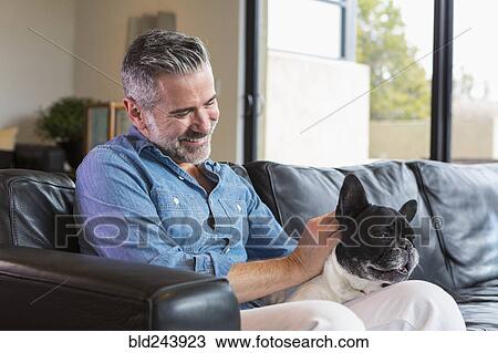 Caucasian man sitting on sofa petting dog View Large Photo Image Stock Image - Caucasian man sitting on sofa petting dog. Fotosearch