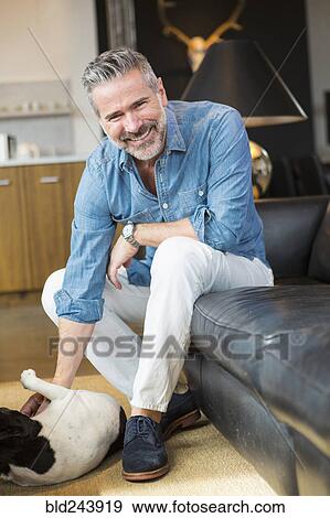 Caucasian man sitting on sofa petting dog View Large Photo Image Stock Photo - Caucasian man sitting on sofa petting dog. Fotosearch