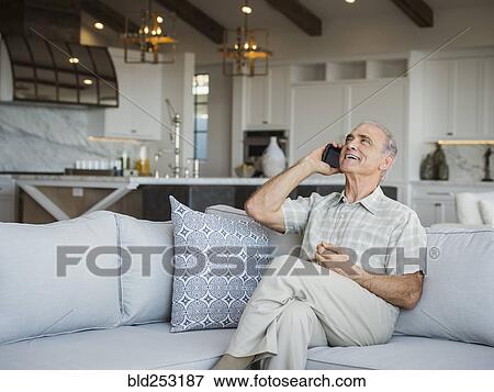 Stock Photo - Caucasian man sitting on sofa talking on cell phone. Fotosearch