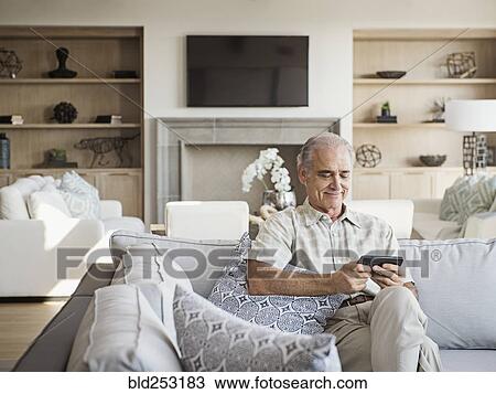 Stock Image - Caucasian man sitting on sofa texting on cell phone. Fotosearch