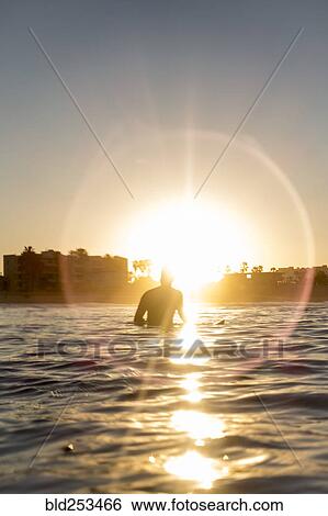 Stock Photograph - Caucasian man sitting on surfboard in ocean. Fotosearch