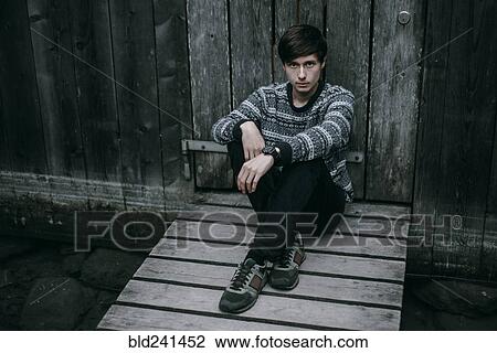 Stock Image - Caucasian man sitting on wooden dock. Fotosearch