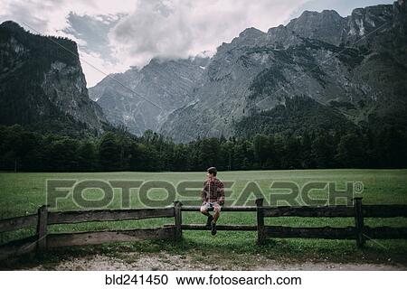 Caucasian man sitting on wooden fence near mountains View Large Photo Image Stock Image - Caucasian man sitting on wooden fence near mountains. Fotosearch