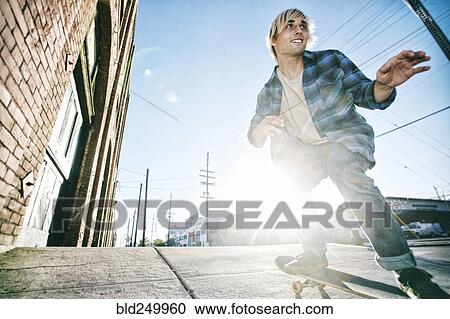 Stock Image - Caucasian man skateboarding on urban sidewalk. Fotosearch