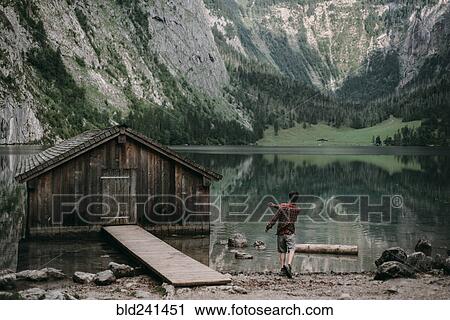 Stock Image - Caucasian man skipping stones in mountain lake. Fotosearch