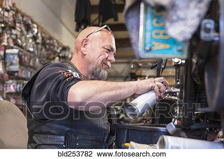 Stock Image - Caucasian man spraying lubricant on motorcycle. Fotosearch