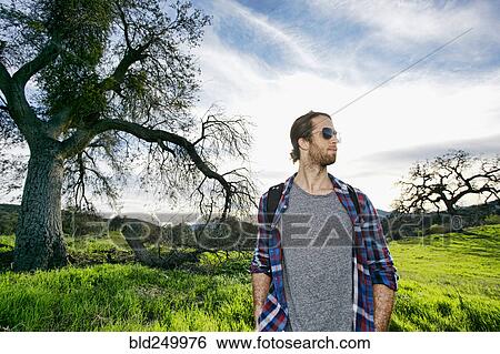 Caucasian man standing in field near tree View Large Photo Image Stock Photograph - Caucasian man standing in field near tree. Fotosearch