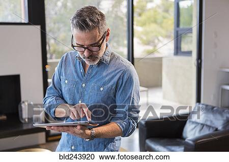 Caucasian man standing in livingroom using digital tablet View Large Photo Image Stock Image - Caucasian man standing in livingroom using digital tablet. Fotosearch