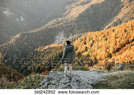 Stock Image - Caucasian man standing on mountain rock overlooking valley. Fotosearch