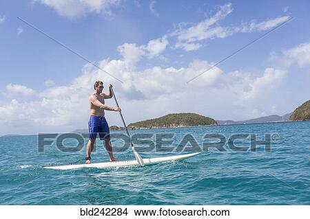 Picture - Caucasian man standing on paddle board on ocean. Fotosearch