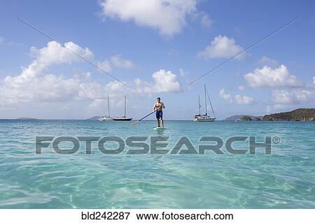 Stock Photo - Caucasian man standing on paddle board on ocean. Fotosearch