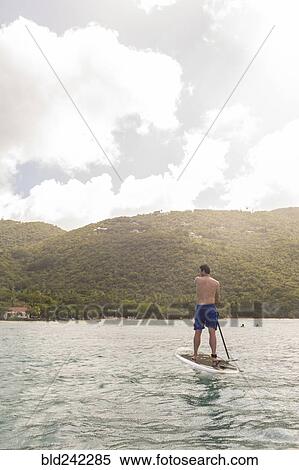 Stock Photography - Caucasian man standing on paddle board on ocean. Fotosearch