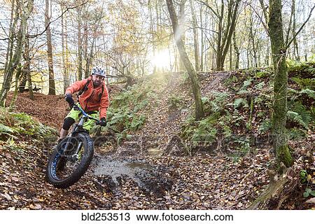 Stock Image - Caucasian man steering bicycle around mud puddle. Fotosearch