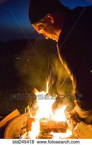 Stock Photo - Caucasian man stoking campfire at night. Fotosearch