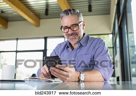 Stock Photo - Caucasian man texting on cell phone at table. Fotosearch
