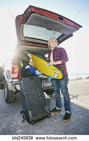 Stock Photo - Caucasian man unloading surfboard from car hatch. Fotosearch