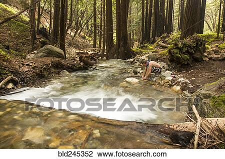 Stock Image - Caucasian man washing foot in forest river. Fotosearch