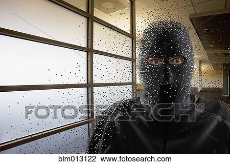 Stock Image - Caucasian man wearing balaclava in office. Fotosearch