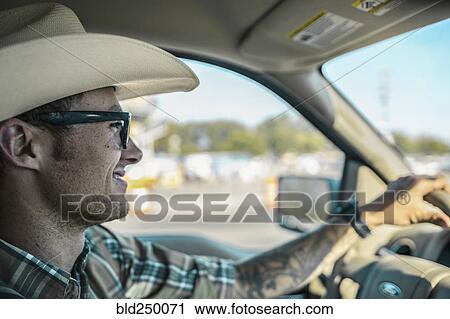 Stock Image - Caucasian man wearing cowboy hat driving car. Fotosearch