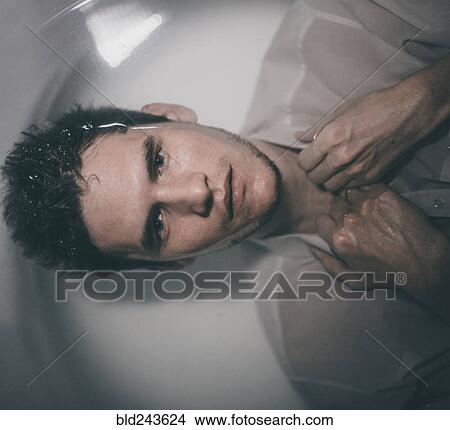 Picture - Caucasian man wearing shirt laying underwater in bathtub. Fotosearch