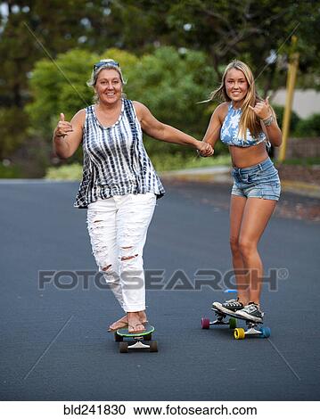 Stock Image - Caucasian mother and daughter holding hands while skateboarding. Fotosearch