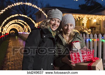 Stock Photo - Caucasian mother and daughter holding Christmas gifts on sidewalk. Fotosearch