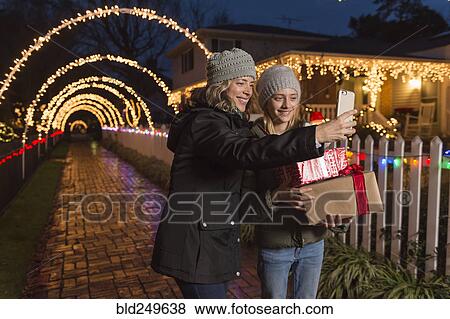 Stock Photo - Caucasian mother and daughter holding Christmas gifts posing for selfie. Fotosearch