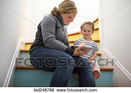 Stock Photo - Caucasian mother and daughter using digital tablet on staircase. Fotosearch