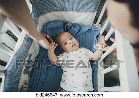 Caucasian mother and father holding hands of baby son in crib View Large Photo Image Stock Photo - Caucasian mother and father holding hands of baby son in crib. Fotosearch