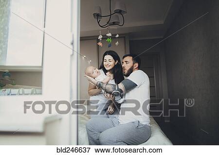 Stock Photo - Caucasian mother and father on bed playing with baby son. Fotosearch