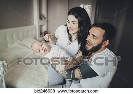 Stock Photo - Caucasian mother and father on bed playing with baby son. Fotosearch