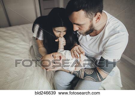 Stock Photo - Caucasian mother and father on bed playing with baby son. Fotosearch