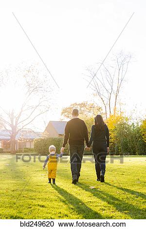 Stock Image - Caucasian mother and father walking in field with son. Fotosearch