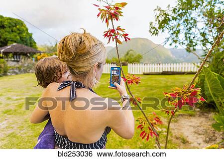 Stock Photograph - Caucasian mother carrying son and photographing with cell phone. Fotosearch