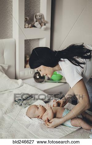 Stock Photo - Caucasian mother changing diaper of baby son on bed. Fotosearch