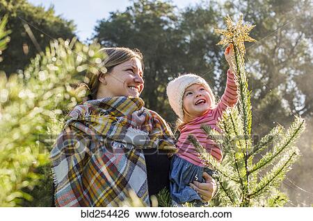 Stock Photograph - Caucasian mother helping daughter place star on top of Christmas tree. Fotosearch