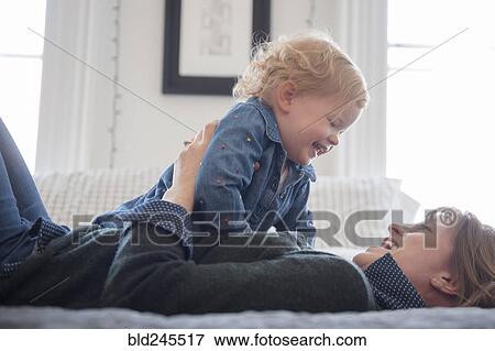 Caucasian mother laying on bed playing with daughter View Large Photo Image Stock Photo - Caucasian mother laying on bed playing with daughter. Fotosearch