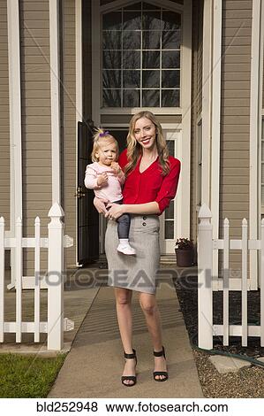 Stock Photo - Caucasian mother posing near house with baby daughter. Fotosearch