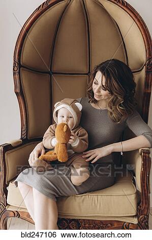 Stock Photograph - Caucasian mother sitting in armchair with baby son wearing bear costume. Fotosearch