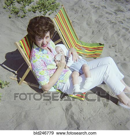 Stock Photo - Caucasian mother sitting on beach feeding bottle to baby son. Fotosearch