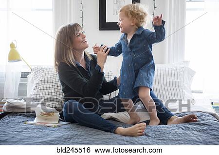 Caucasian mother sitting on bed playing with daughter View Large Photo Image Stock Photograph - Caucasian mother sitting on bed playing with daughter. Fotosearch