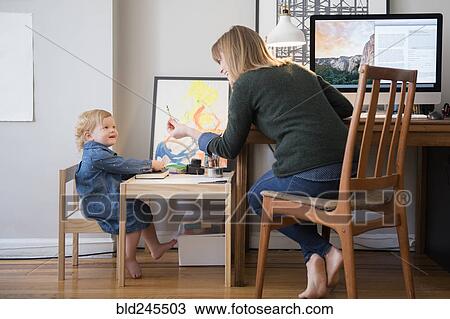 Stock Image - Caucasian mother working and daughter playing in home office. Fotosearch