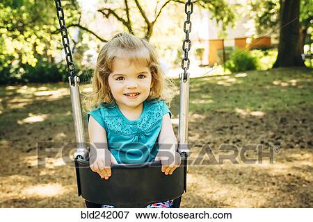 Stock Photo - Caucasian preschool girl sitting in swing. Fotosearch
