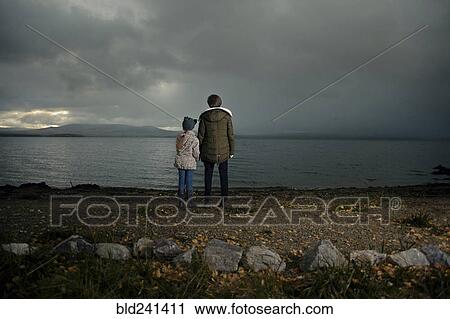 Stock Image - Caucasian sisters holding hands at lake. Fotosearch
