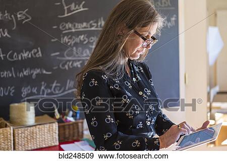 Stock Photo - Caucasian teacher using digital tablet in classroom. Fotosearch