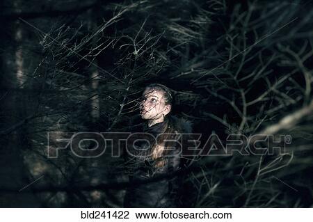 Stock Image - Caucasian teenage girl behind tree branches at night. Fotosearch