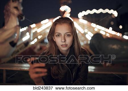 Stock Photo - Caucasian teenage girl holding cell phone at amusement park. Fotosearch