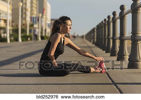 Stock Photograph - Caucasian teenage girl sitting on boardwalk stretching legs. Fotosearch
