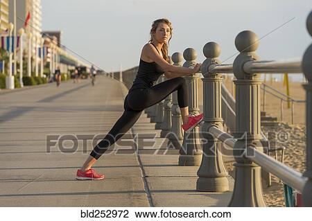Stock Image - Caucasian teenage girl stretching leg on railing at beach. Fotosearch